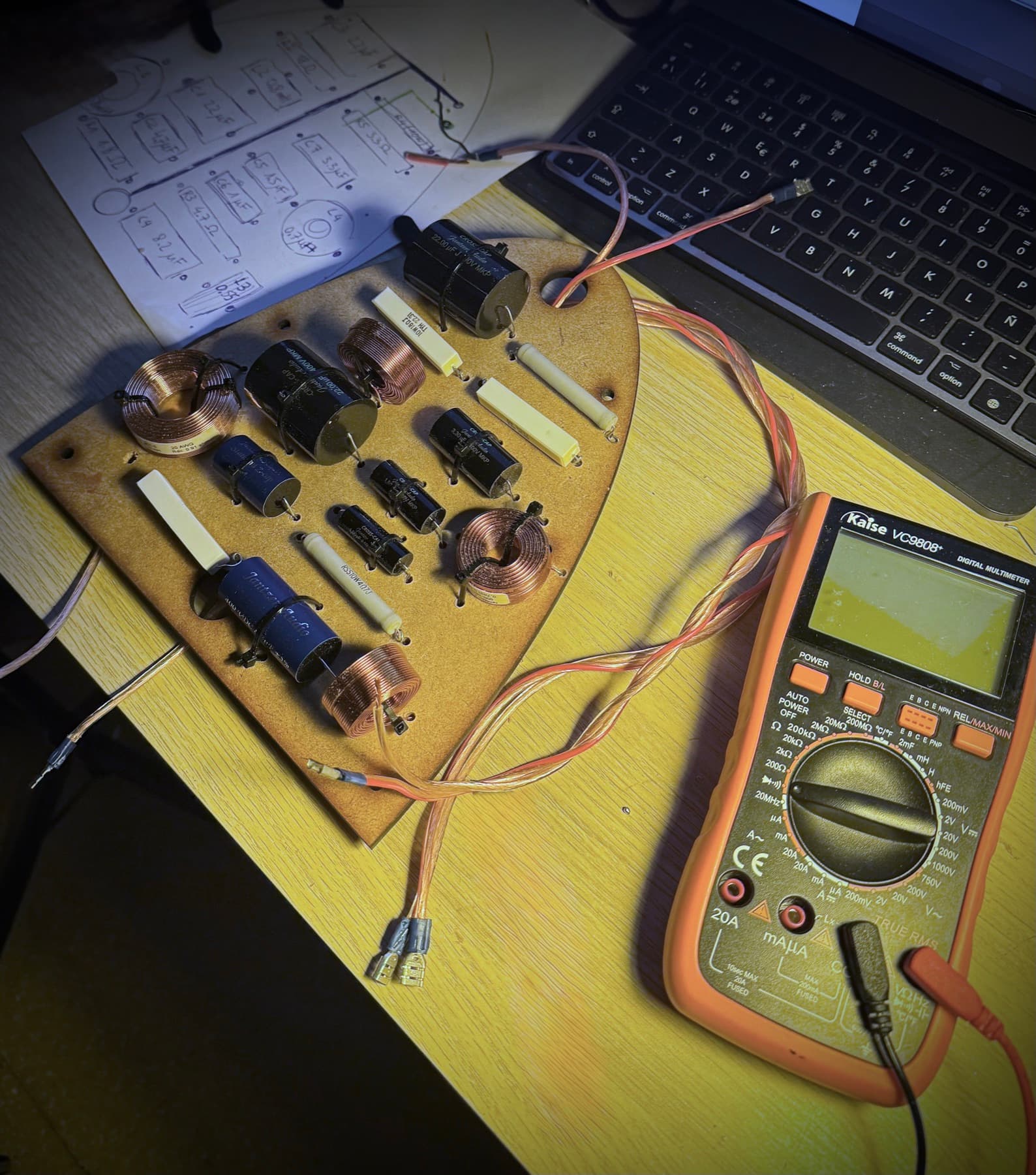 Assembled crossover on its board, with a multimeter beside it